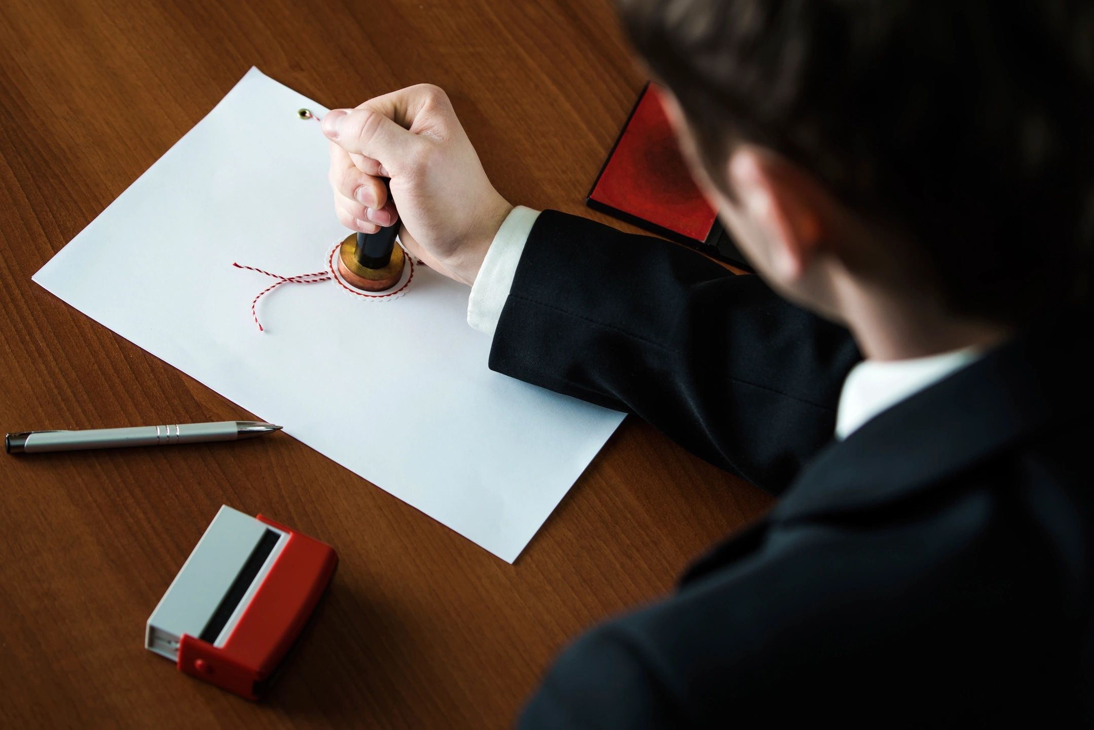 Person sealing a document with wax and a stamp on a wooden desk.